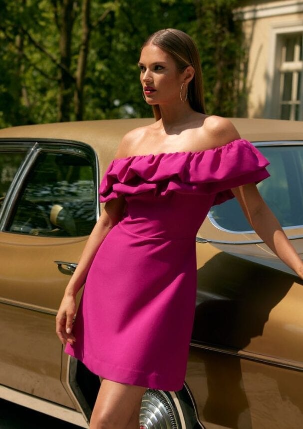 sukienka mini w fuksjowym kolorze z falbaną przy ramionach, modelka ma na sobie również dodatek w postaci kolczyków