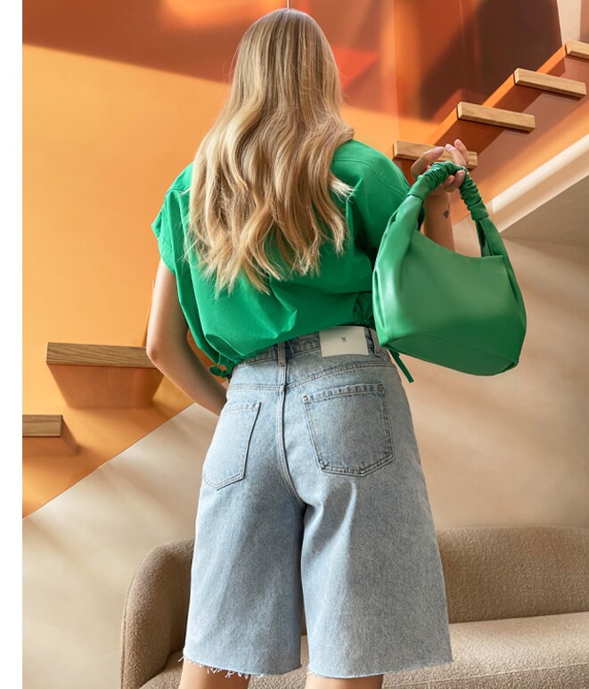 dziewczyna z długimi, jasnymi włosami w stylizacji typu zielona koszula oversize i jeansowe spodenki, bermudy