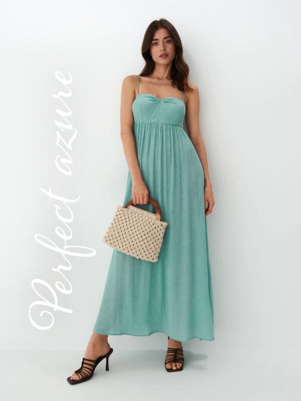 modelka w turkusowej sukience maxi z pleciona torebką do ręki oraz klapkami na obcasie 
