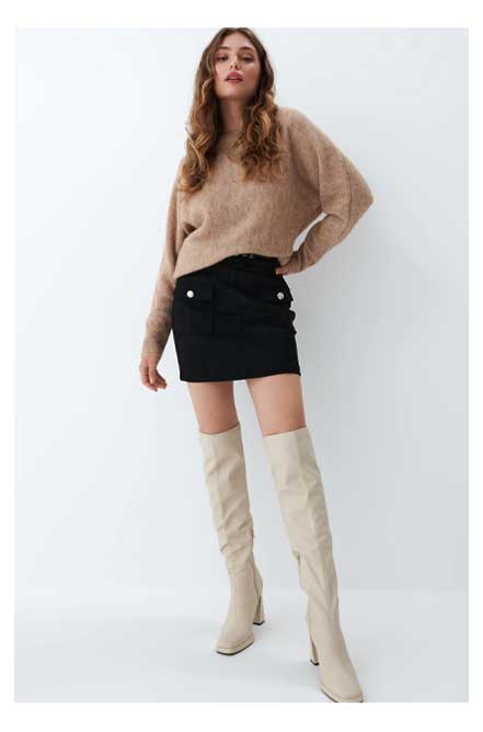 modelka w stylizacji jesienno-zimowej - beżowy sweter, spódnica mini czarna i jasne wysokie kozaki na obcasie
