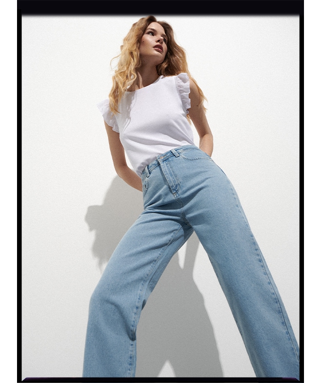 modelka w szerokich spodniach jeansowych i białej bluzce z falbanami