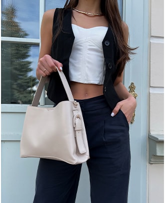 modelka w stylizacji z białym topem, czarną kamizelką oraz szerokimi spodniami i kremową torebką