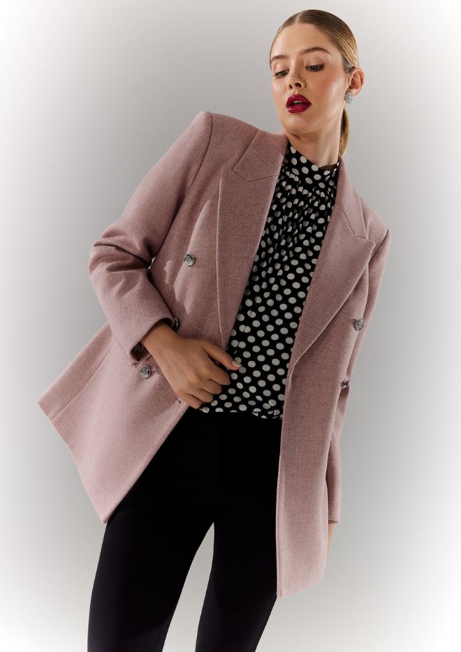 îmbracă o jachetă roz voluminoasă și o bluză cu buline