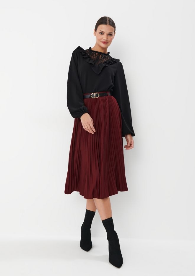 modelka w plisowanej spódnicy midi i czarnej bluzce oraz botkach