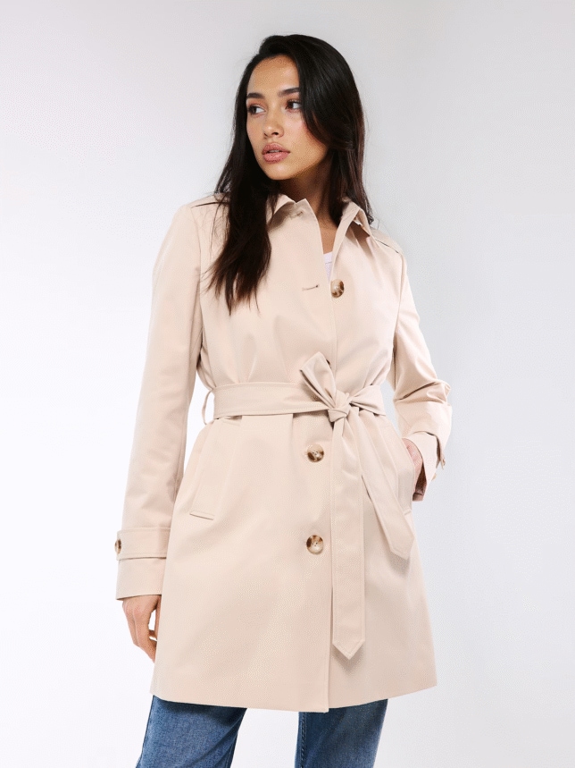 Modelka w beżowym trencze przewiązanym w talii i niebieskich jeansach; idealna lekka stylizacja na walentynkowy spacer.