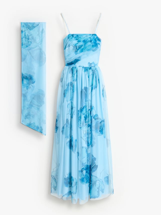 Sukienka o kroju litery A i długości maxi, z ozdobnym szalem na szyi.
Niebieska sukienka dla świadkowej w kwiaty z szalem.