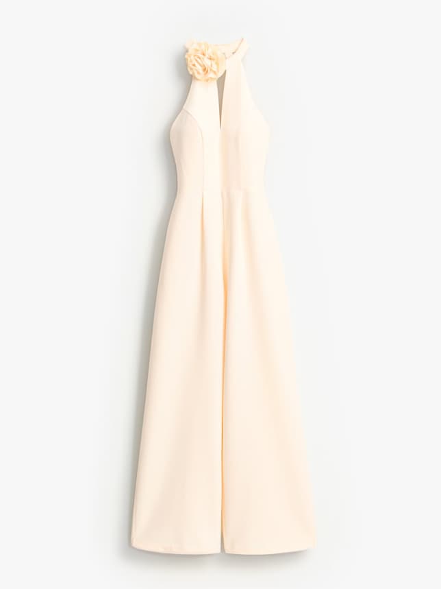 Kombinezon z ozdobnym kwiatem 3D. Posiada wycięcie przy dekolcie i długie nogawki. Idealna kreacja na wesele 2026.
