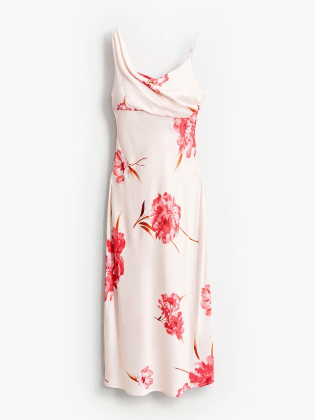 Satynowa sukienka midi na wesele o bieliźnianym kroju (slip dress). Kreacja ma cienkie ramiączka, lejący dekolt i jest wykonana z błyszczącej tkaniny w kolorze ecru z rozmieszczonymi gdzieniegdzie nadrukami dużych, różowych kwiatów piwonii.