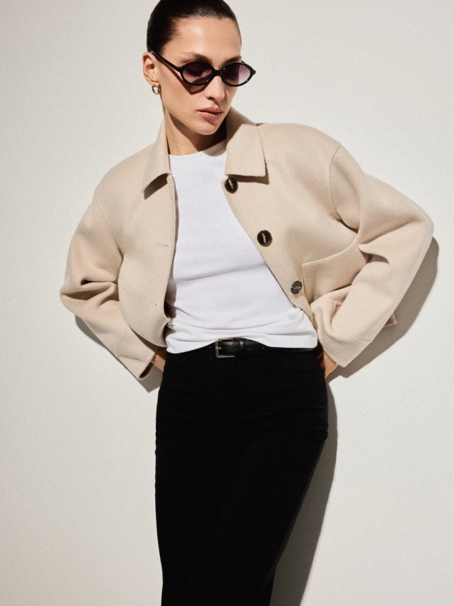 Krótka kurtka z wełną w kolorze beżowym wystylizowana z białą koszulką, czarnymi spodniami, czarnymi okularami przeciwsłonecznymi 