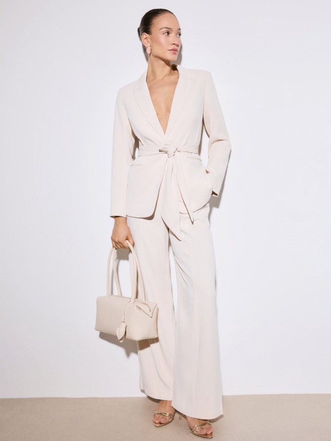 Monochromatyczna stylizacja na wesele: marynarka z dekoltem w serek i ozdobnym wiązaniem, zestawiona ze spodniami typu wide-leg i złotymi sandałkami.