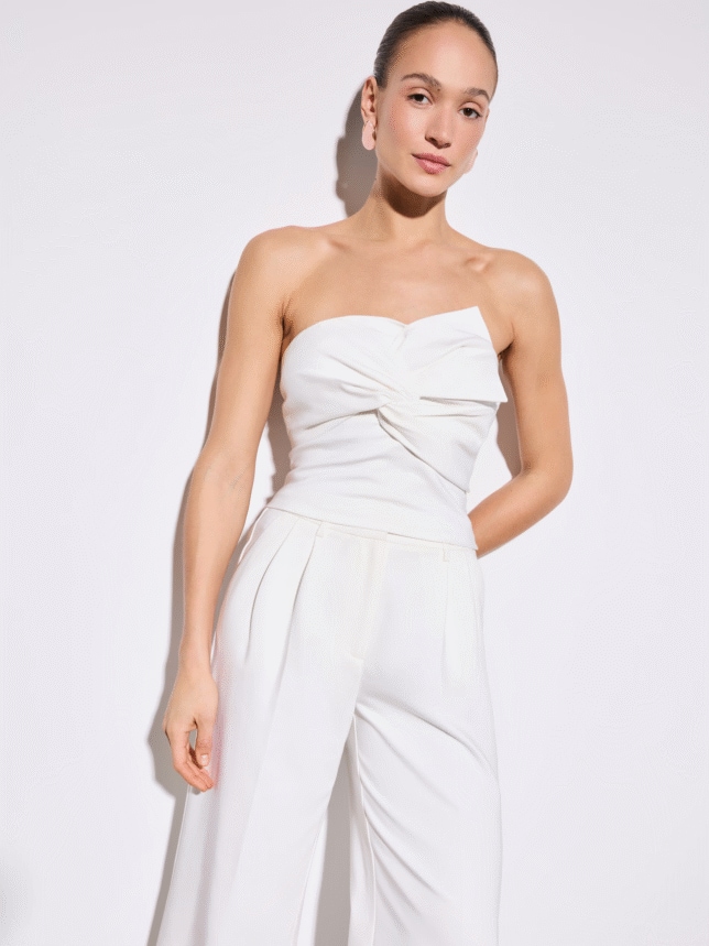 Górna część eleganckiego białego kompletu: dopasowany top bez ramiączek o ciekawej strukturze, zestawiony z delikatną biżuterią.