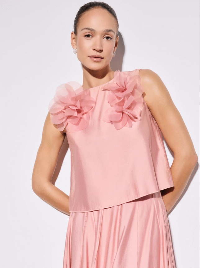 Zbliżenie na różowy top bez rękawów z dużymi, tiulowymi aplikacjami w kształcie kwiatów przy dekolcie.