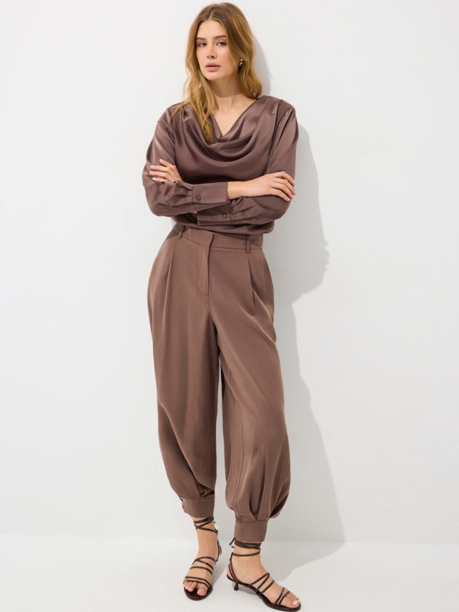 Elegancki brązowy komplet damski: satynowa bluzka z dekoltem typu woda i dopasowane spodnie z bufiastymi nogawkami, zestawione z sandałami na obcasie.