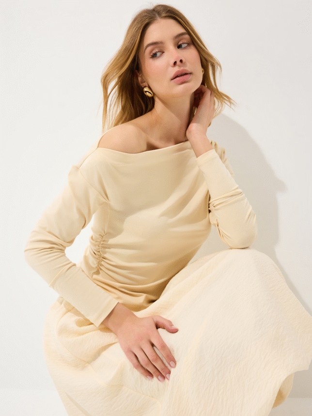 Zbliżenie na waniliowy top z długim rękawem, asymetrycznym dekoltem i dekoracyjnym marszczeniem na boku.