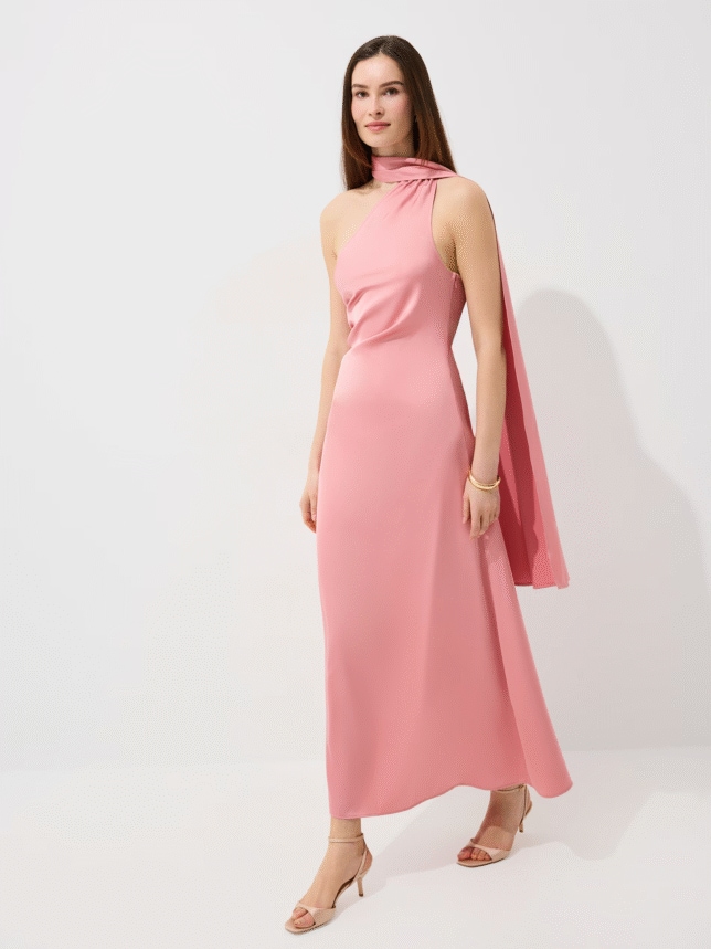 Elegancka wieczorowa stylizacja: modelka w dopasowanej różowej sukni z odkrytym jednym ramieniem i długą szarfą opadającą na plecy, zestawiona z beżowymi sandałkami.