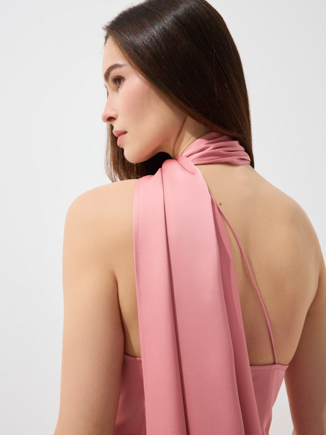 Widok z tyłu na detale sukienki wizytowej: różowa, subtelne ramiączko i efektowne drapowanie szarfy na ramieniu.