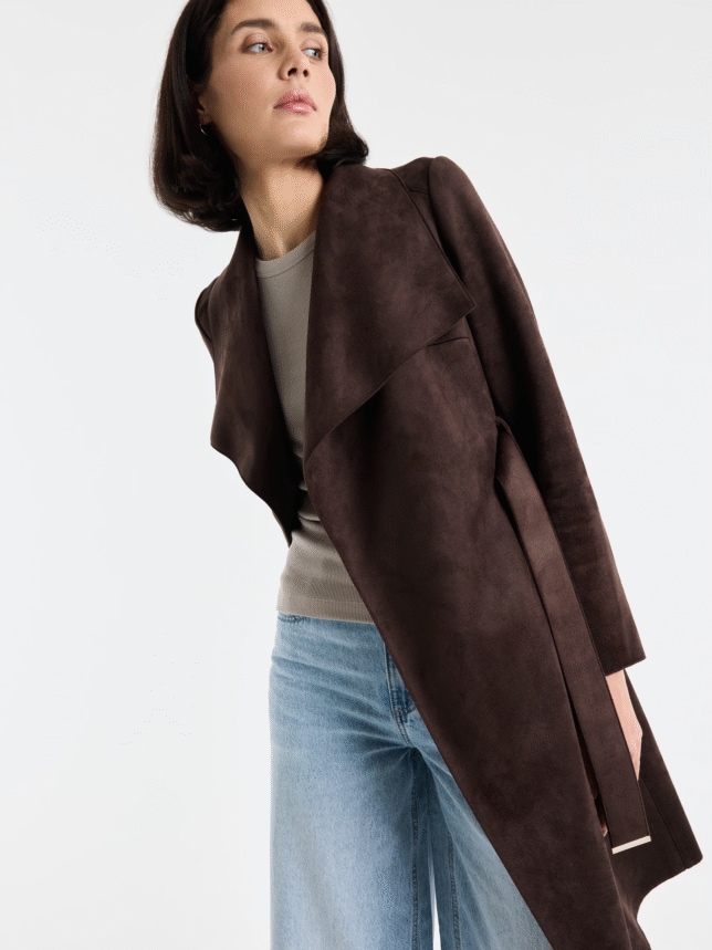 Zbliżenie na górną część sylwetki modelki w ciemnobrązowym płaszczu z szerokimi klapami, prezentujące strukturę materiału imitującego zamsz.