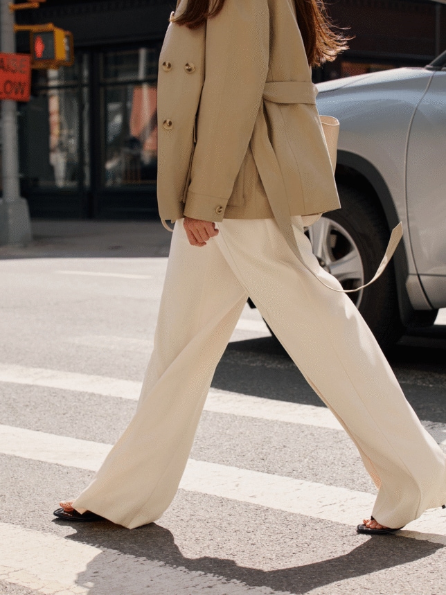 Detale stylizacji old money 2026: perfekcyjnie skrojone, szerokie spodnie palazzo w odcieniu ivory zestawione z beżową marynarką, uchwycone w dynamicznym kroku na miejskiej ulicy.